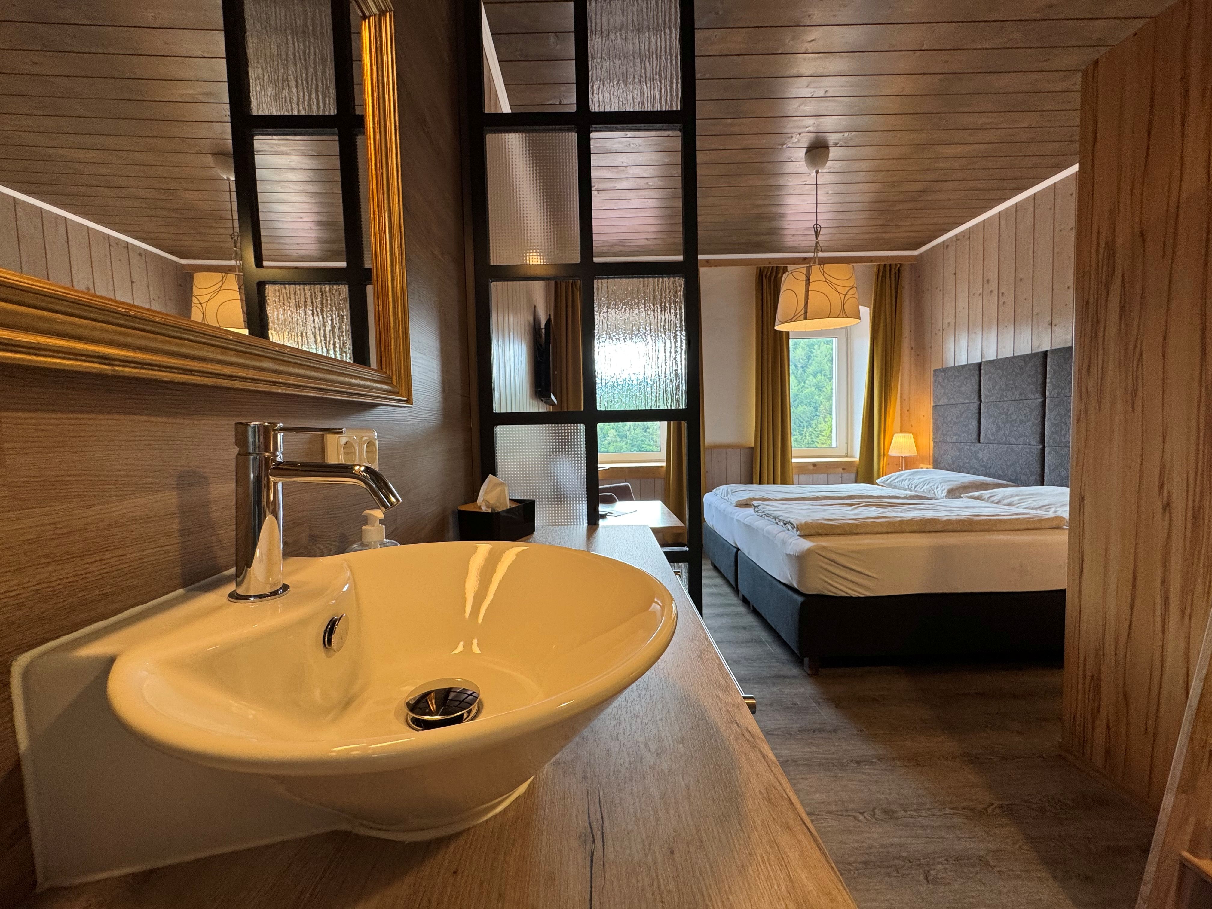 Innenansicht eines gemütlichen Zimmers mit Waschbecken, Doppelbett und Holzverkleidung.