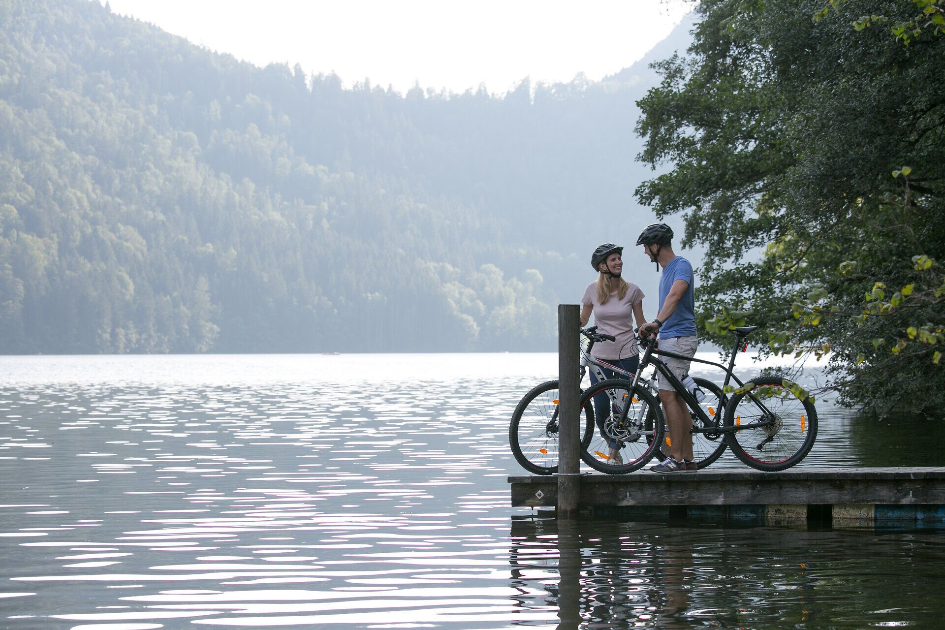 Ein Paar genießt einen romantischen Moment am Ufer eines glitzernden Sees, umgeben von majestätischen Bergen. Die sanften Wellen spiegeln die Schönheit der Natur wider und laden zu unvergesslichen Erlebnissen ein.