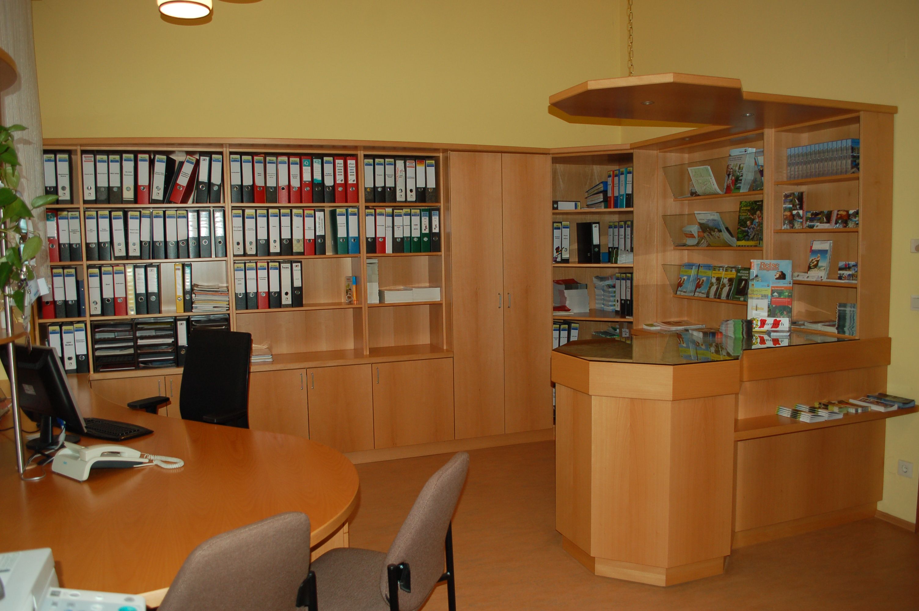 Innenansicht eines Büros mit Holzregalen, Aktenordnern und einem Empfangstresen.