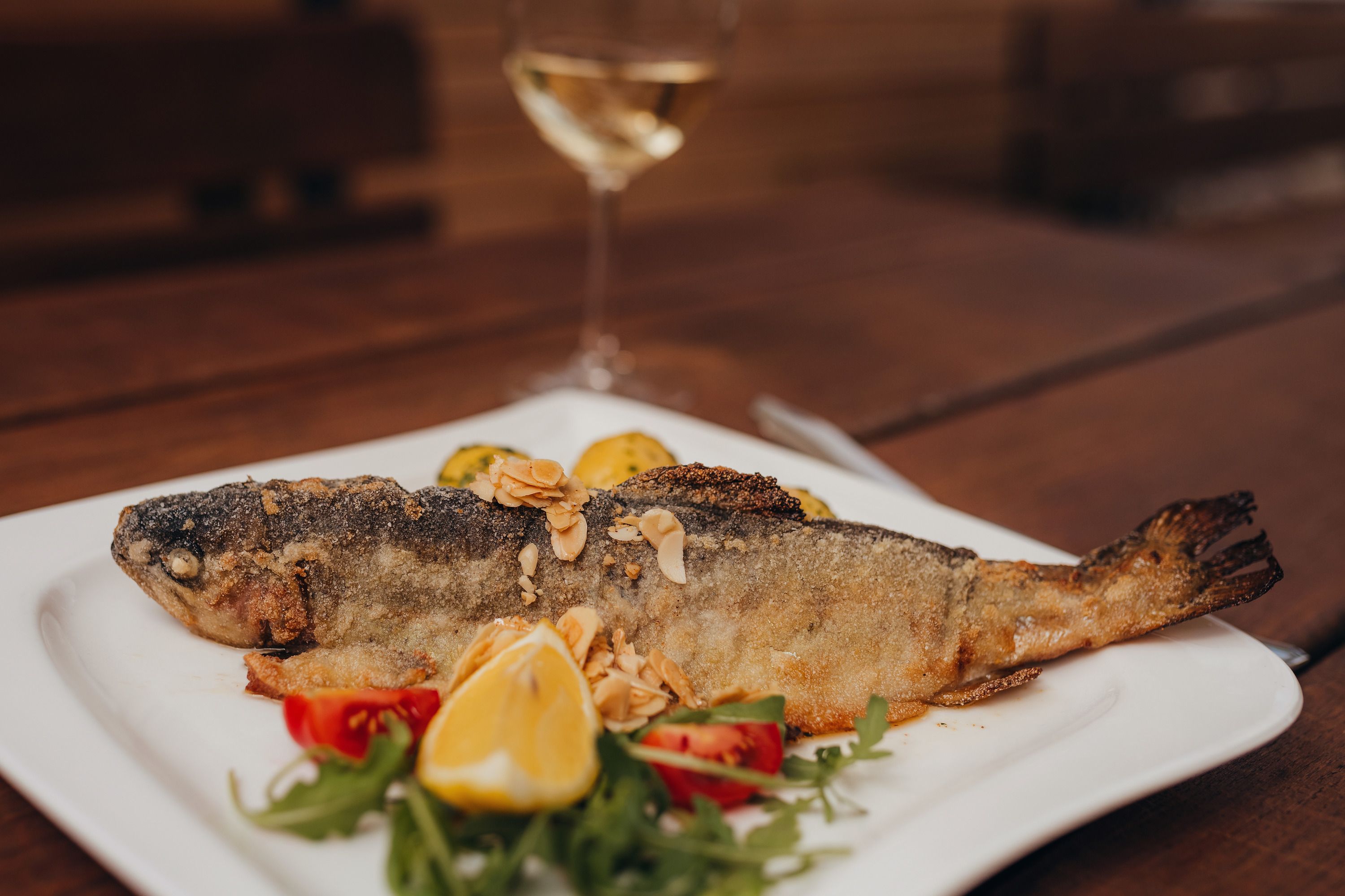 Gebratene Forelle mit Mandelbutter auf einem Teller, garniert mit Zitrone und Gemüse.