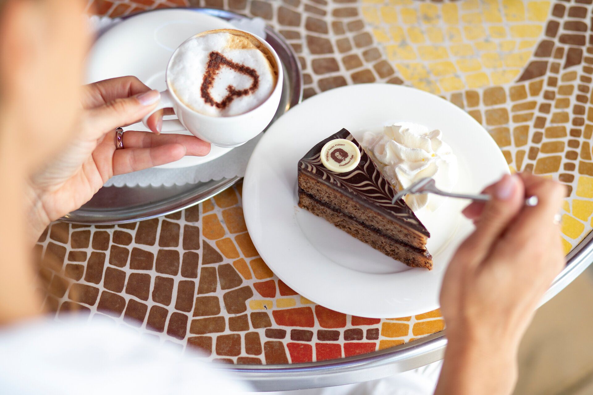 Genießen Sie eine köstliche Tasse Kaffee in einem einladenden Café, während Sie ein Stück schokoladigen Kuchen probieren. Die entspannte Atmosphäre und die liebevolle Präsentation der Speisen laden dazu ein, den Moment in vollen Zügen auszukosten.