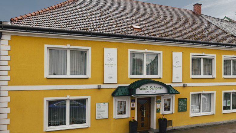 Gelbes Gasthaus mit grüner Markise und mehreren Fenstern.