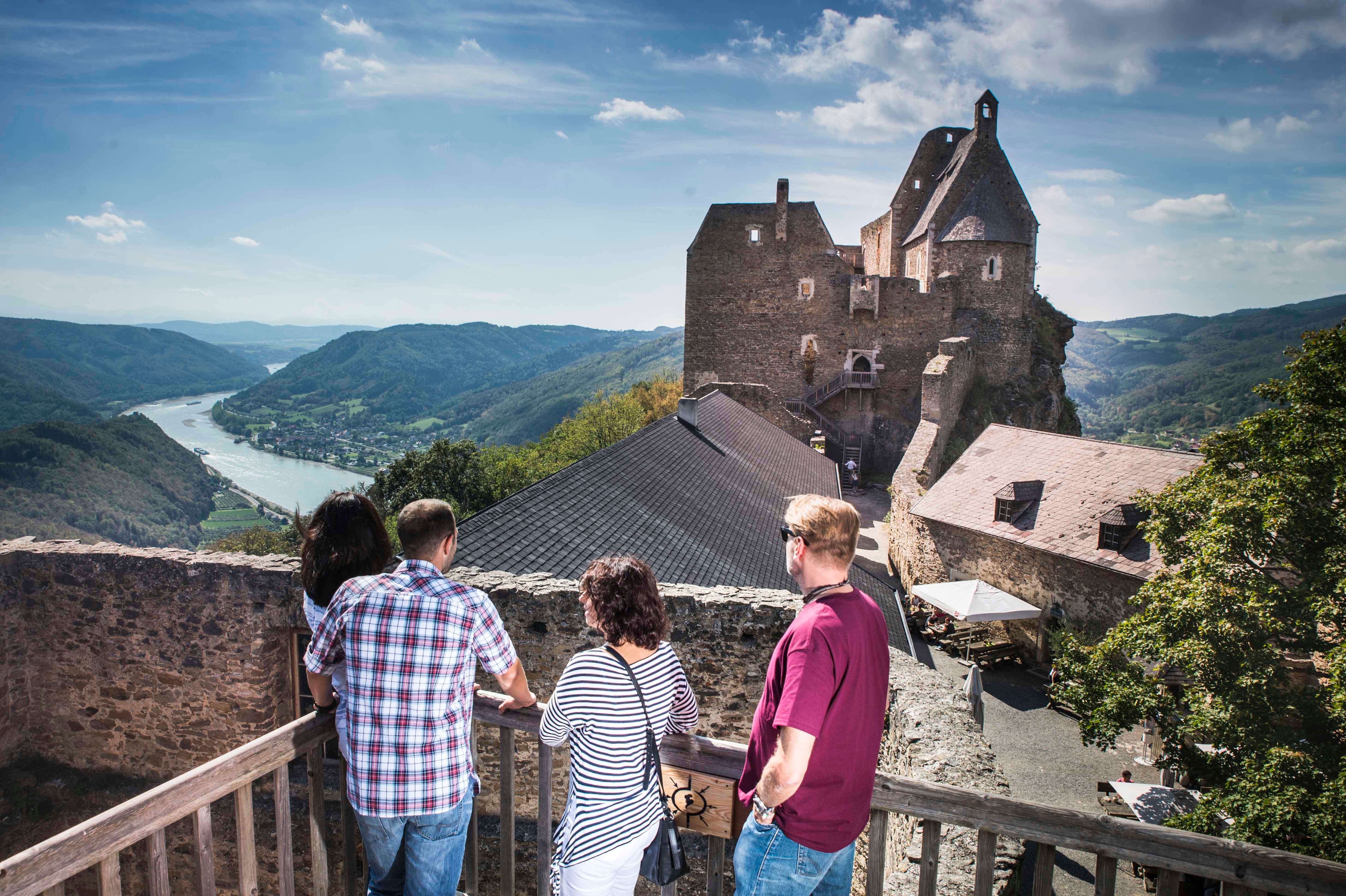 Menschen auf einer Burg mit Blick auf Fluss und Berge.