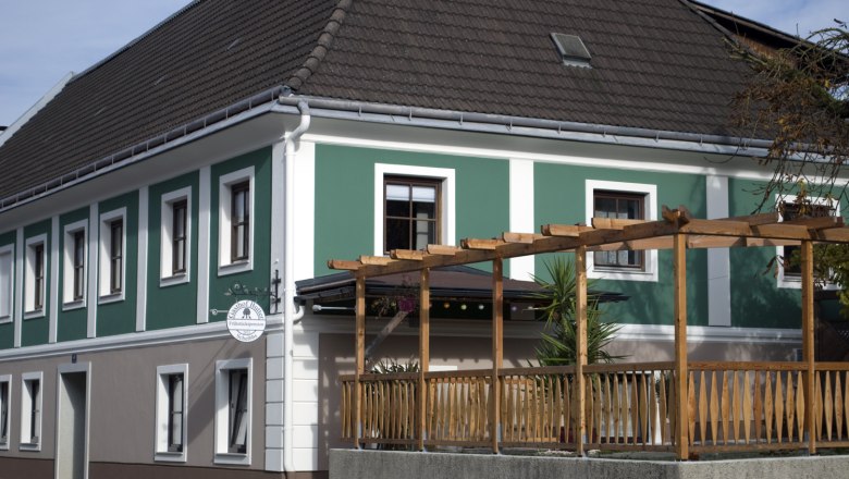Außenansicht einer Frühstückspension mit grün-weißer Fassade und Holzpergola.
