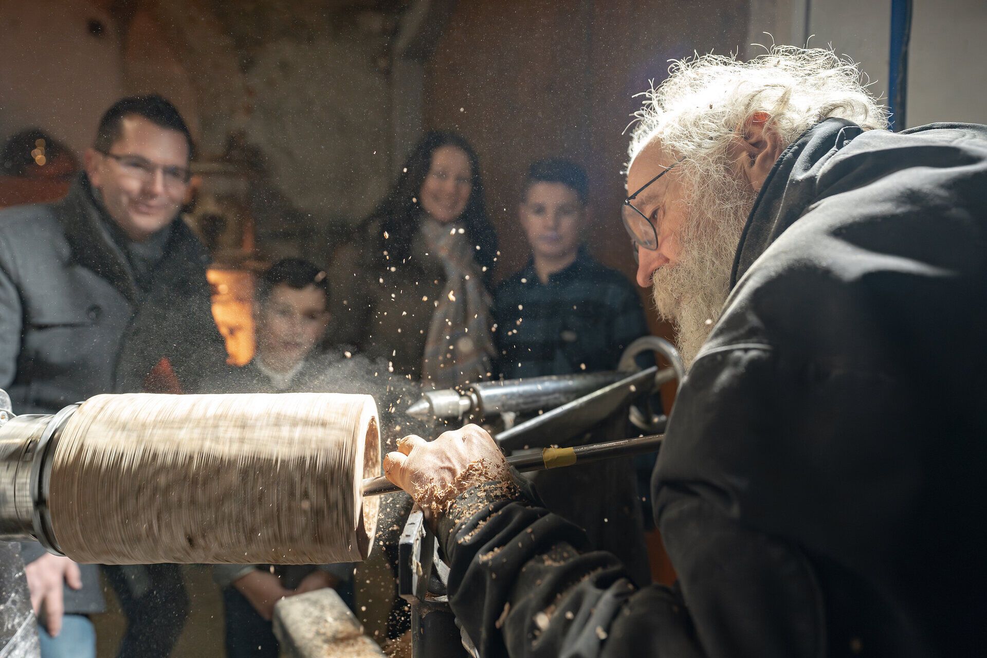 Familie beobachtet Mann bei der Bearbeitung eines Holzstücks.