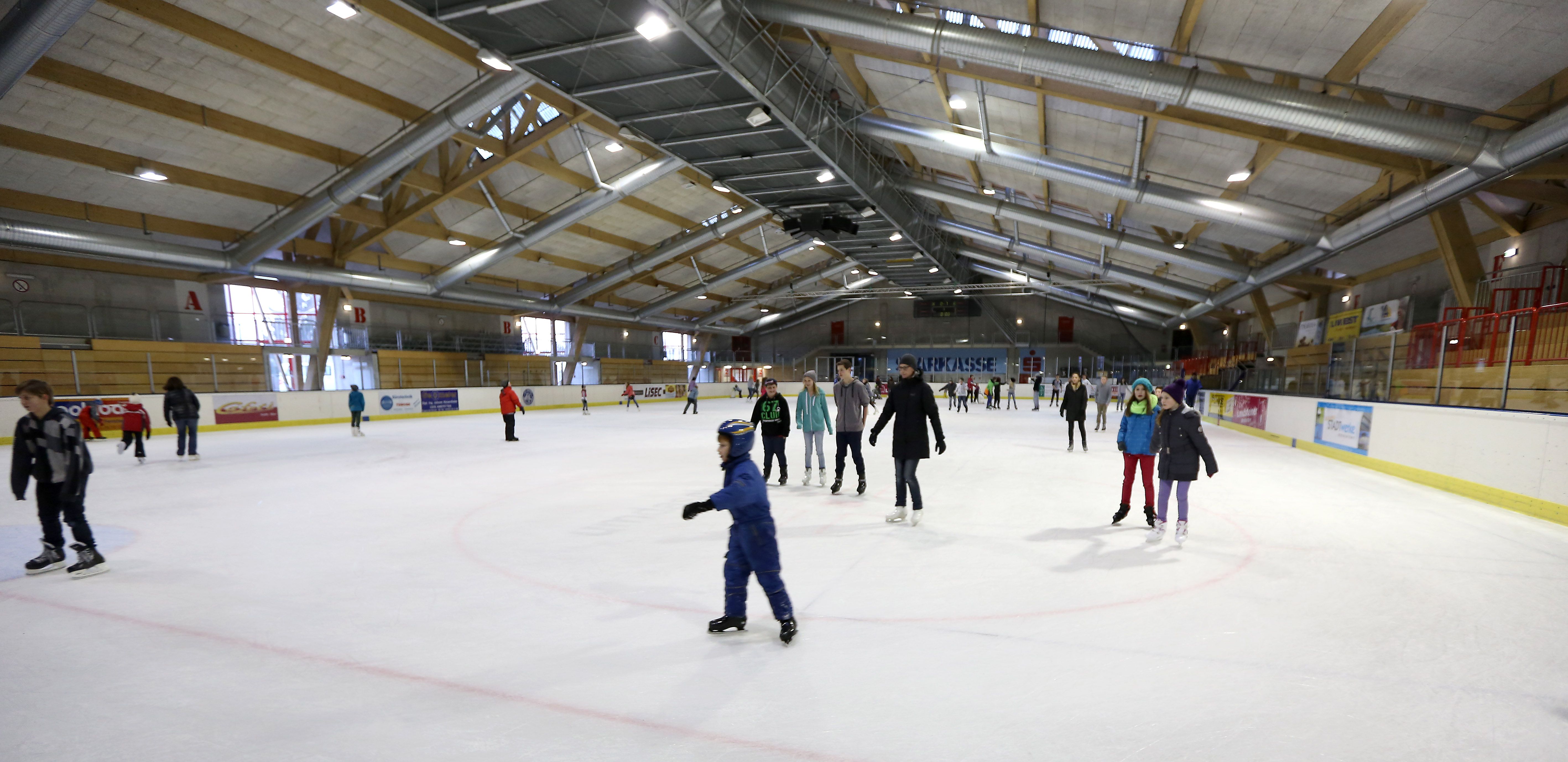 Menschen beim Eislaufen in einer großen Eishalle.