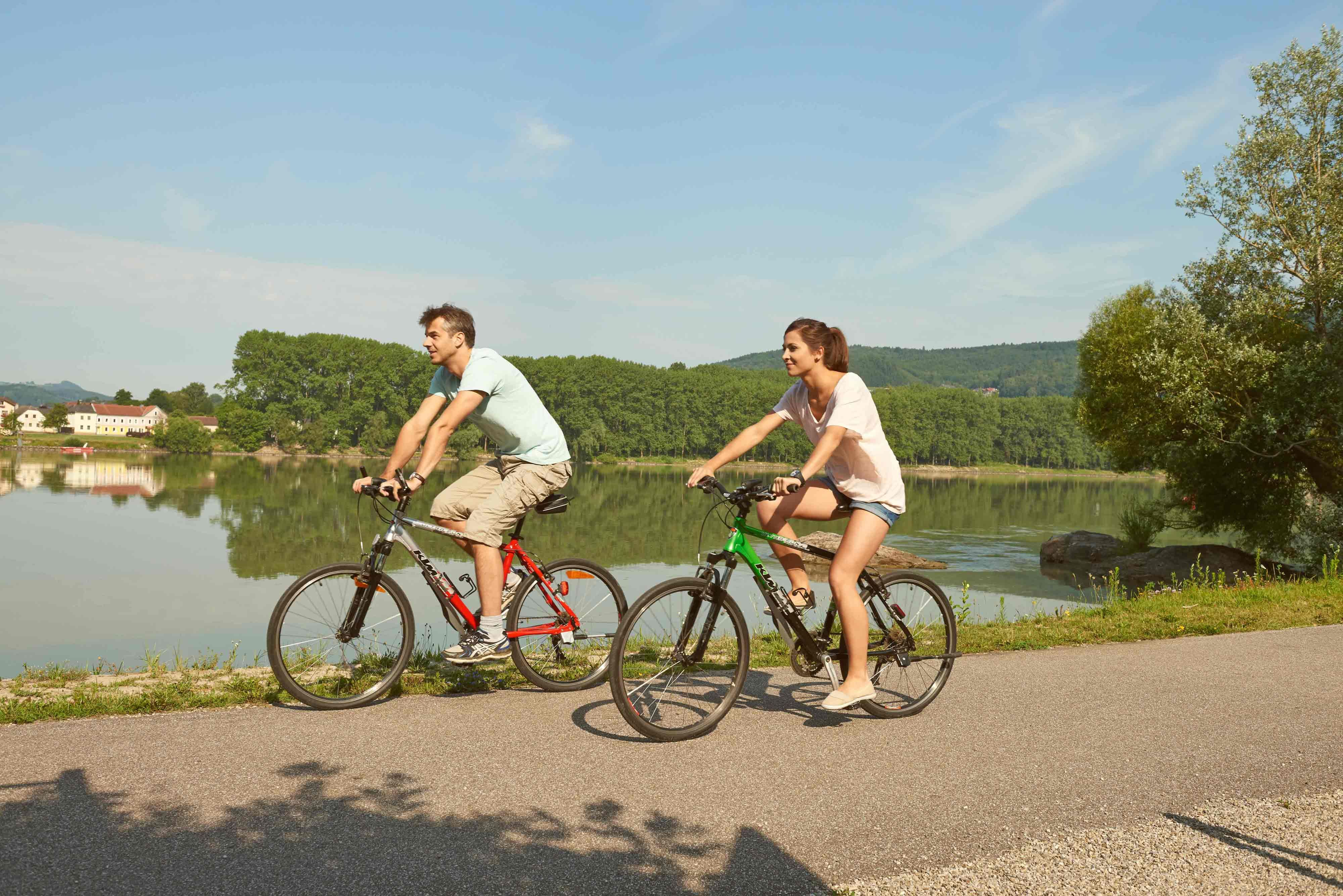 Zwei Radfahrer fahren auf einem Weg entlang eines Flusses im Nibelungengau.