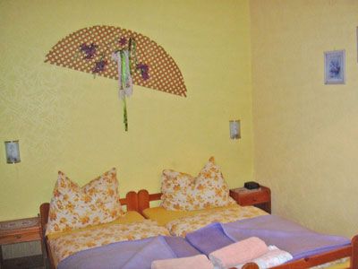 Ein gemütliches Schlafzimmer mit gelben Wänden, einem Doppelbett mit gemusterten Kissen und einem dekorativen Wandfächer.