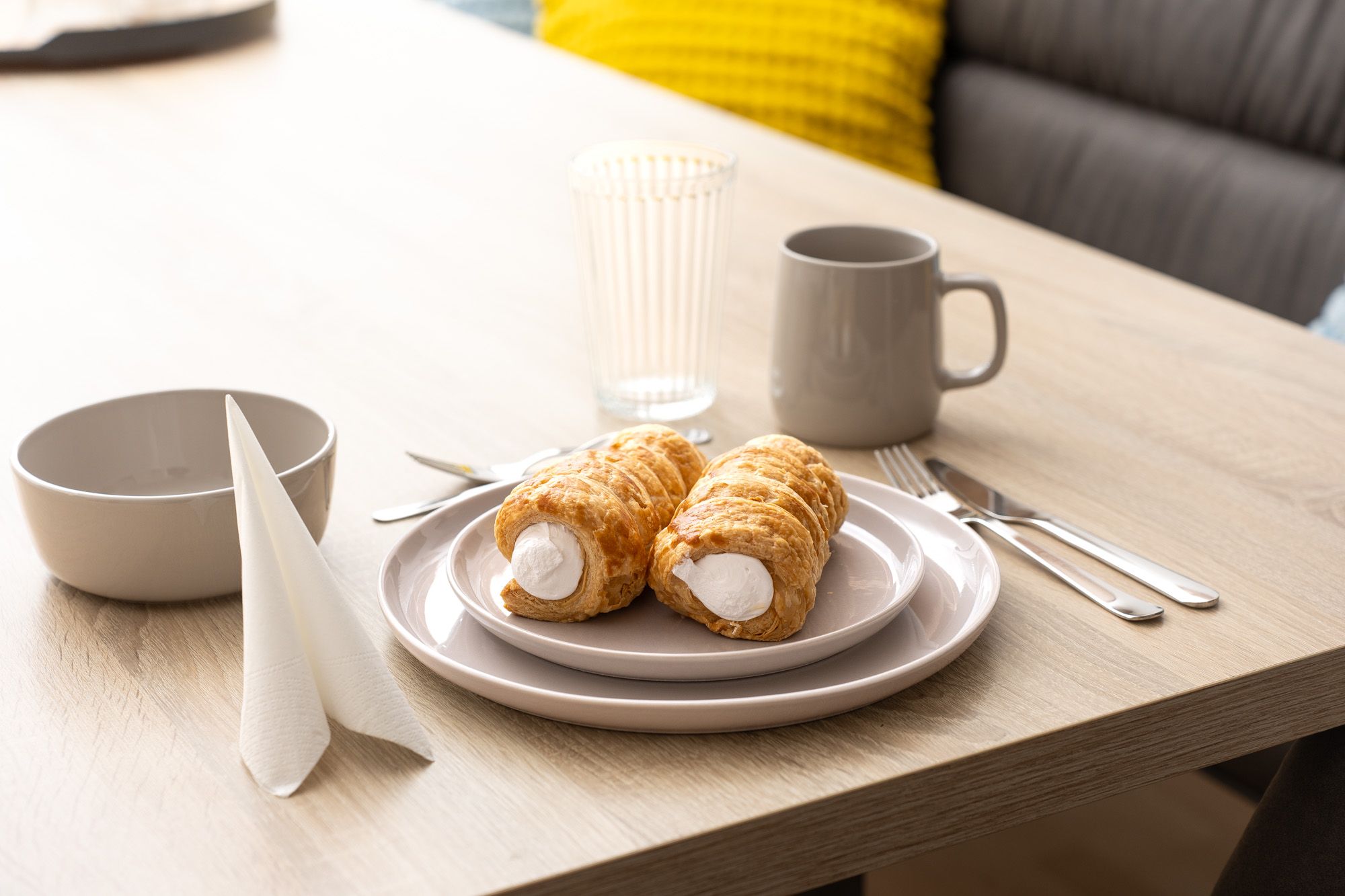 Frühstückstisch in der Ferienwohnung Turmblick mit zwei Schaumrollen, Geschirr und Tassen auf hellem Holztisch.