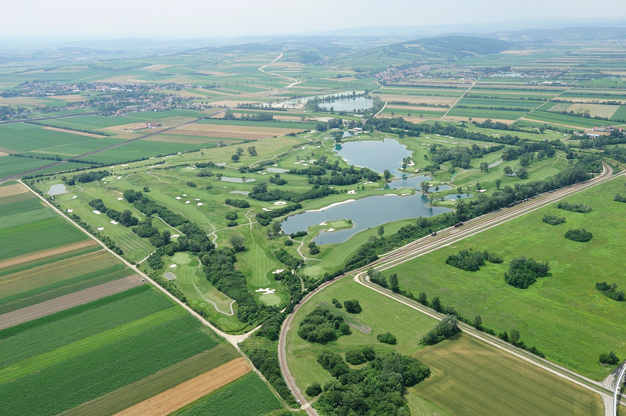 Luftaufnahme eines Golfplatzes mit Seen und umliegenden Feldern.