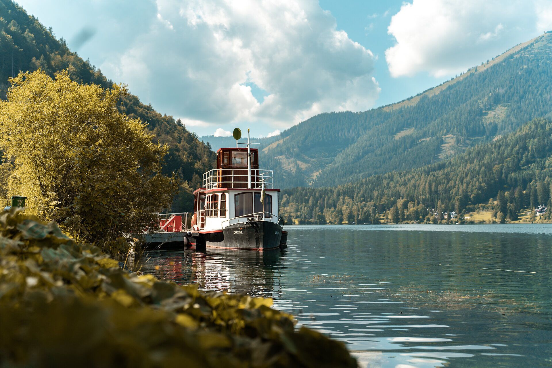 Der glitzernde Erlaufsee spiegelt die majestätischen Berge wider, während sanfte Wellen das Ufer umspielen. Umgeben von üppigem Grün und goldenen Blättern, lädt dieser Ort zum Entspannen und Verweilen ein. Hier erleben Besucher die harmonische Verbindung von Natur und Ruhe.