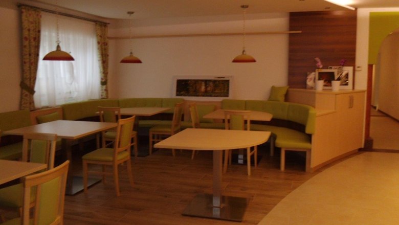 Innenansicht eines Cafés mit grünen Sitzbänken und Holztischen.