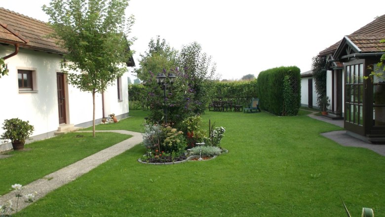Very well-kept garden with a view of shrubs and trees, with part of the building in the background.