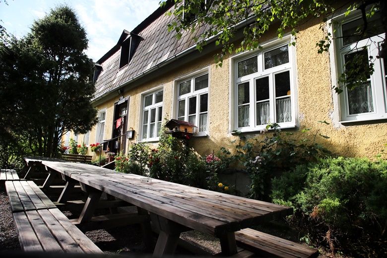 Gelbes Gebäude mit weißen Fenstern und langen Holzbänken im Vordergrund.