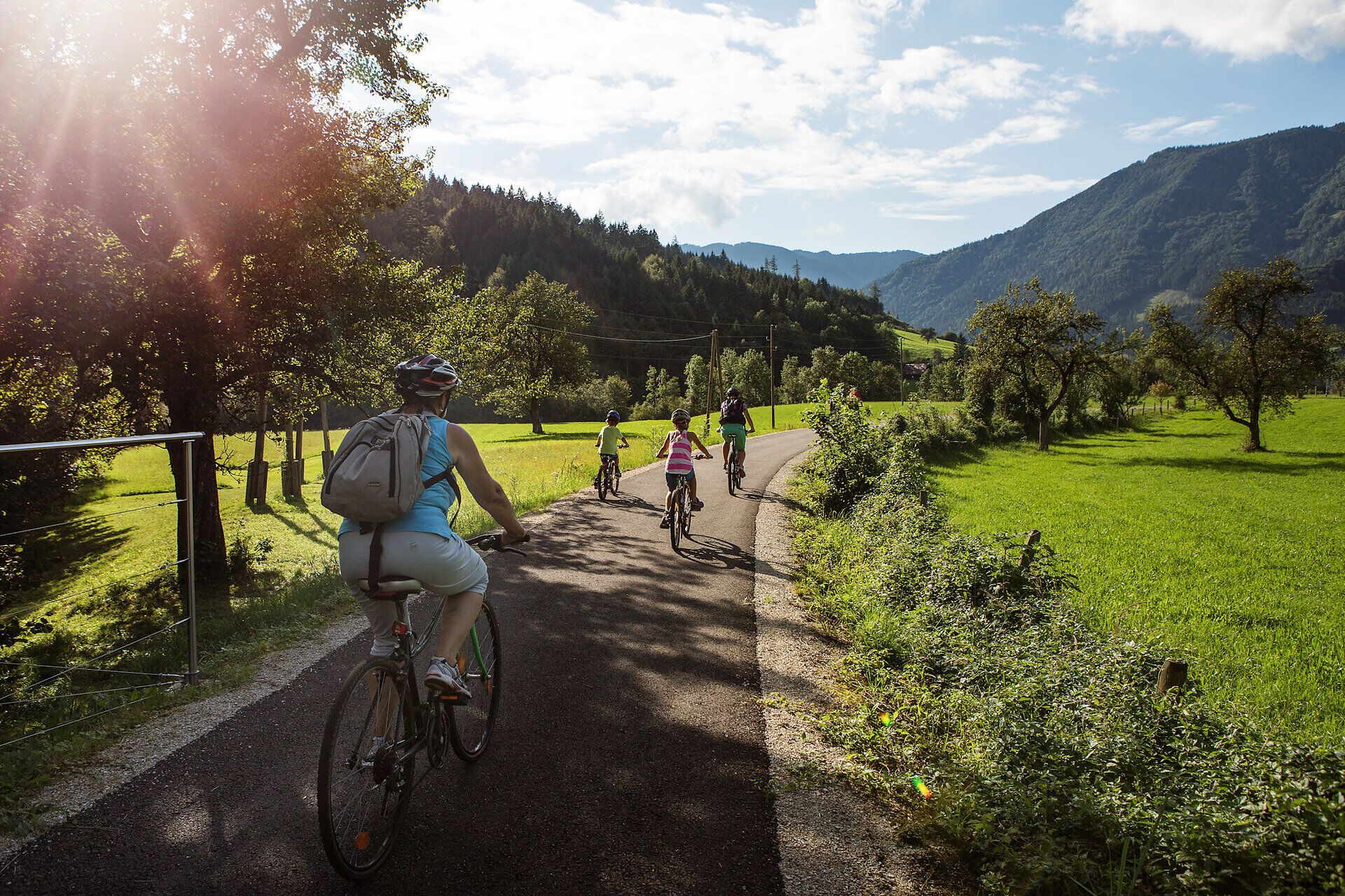 Eine Familie genießt einen sonnigen Tag auf dem Ybbstalradweg, umgeben von üppigem Grün und majestätischen Bergen. Die frische Luft und die sanften Hügel laden zu unvergesslichen Fahrradtouren ein, während die Kinder fröhlich lachen und die Natur erkunden.