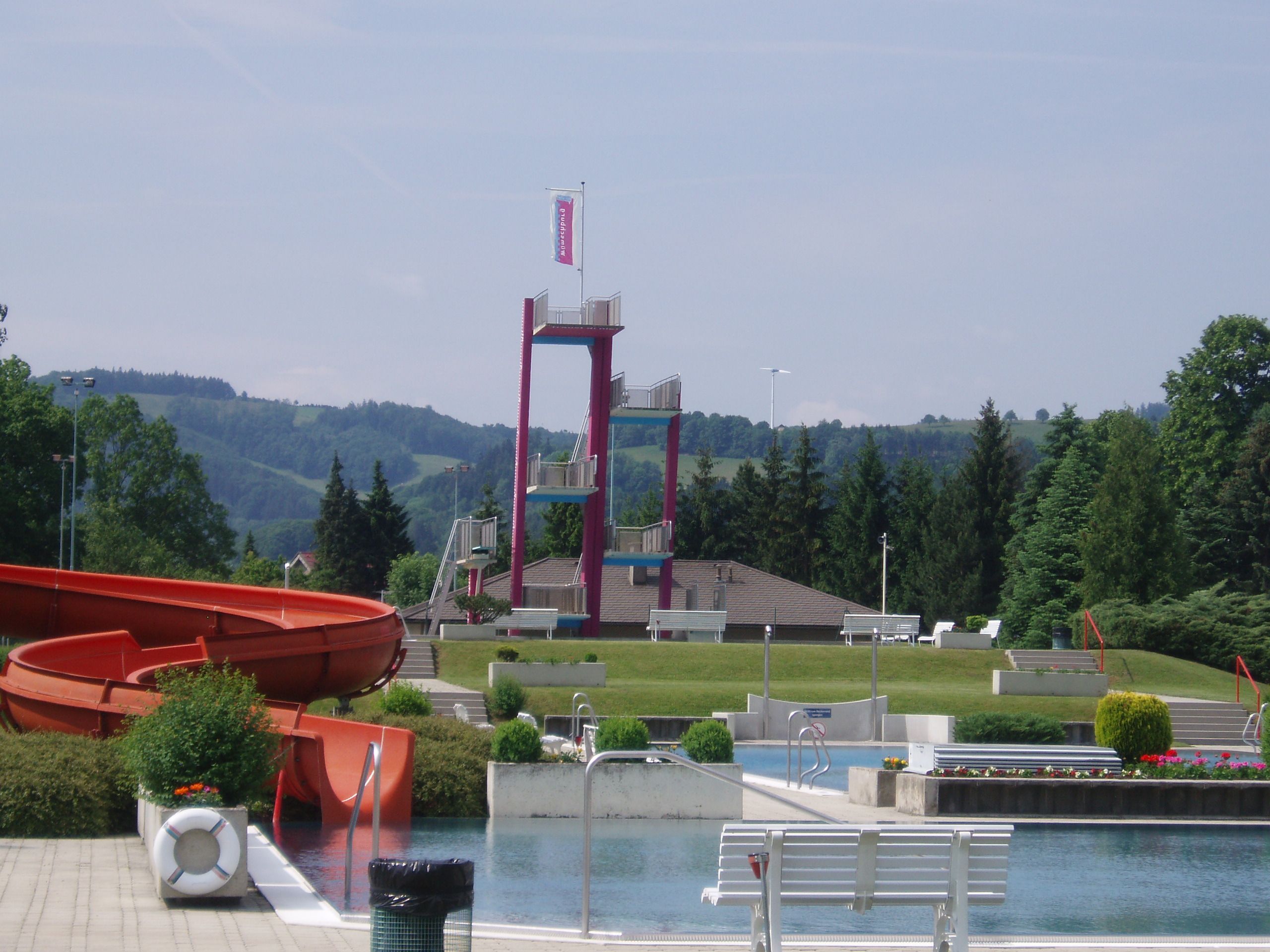 Ein Freibad mit Rutsche, Sprungturm und grüner Umgebung.