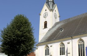 Stadtpfarrkirche St. Laurenz mit Turm und Uhr vor blauem Himmel.