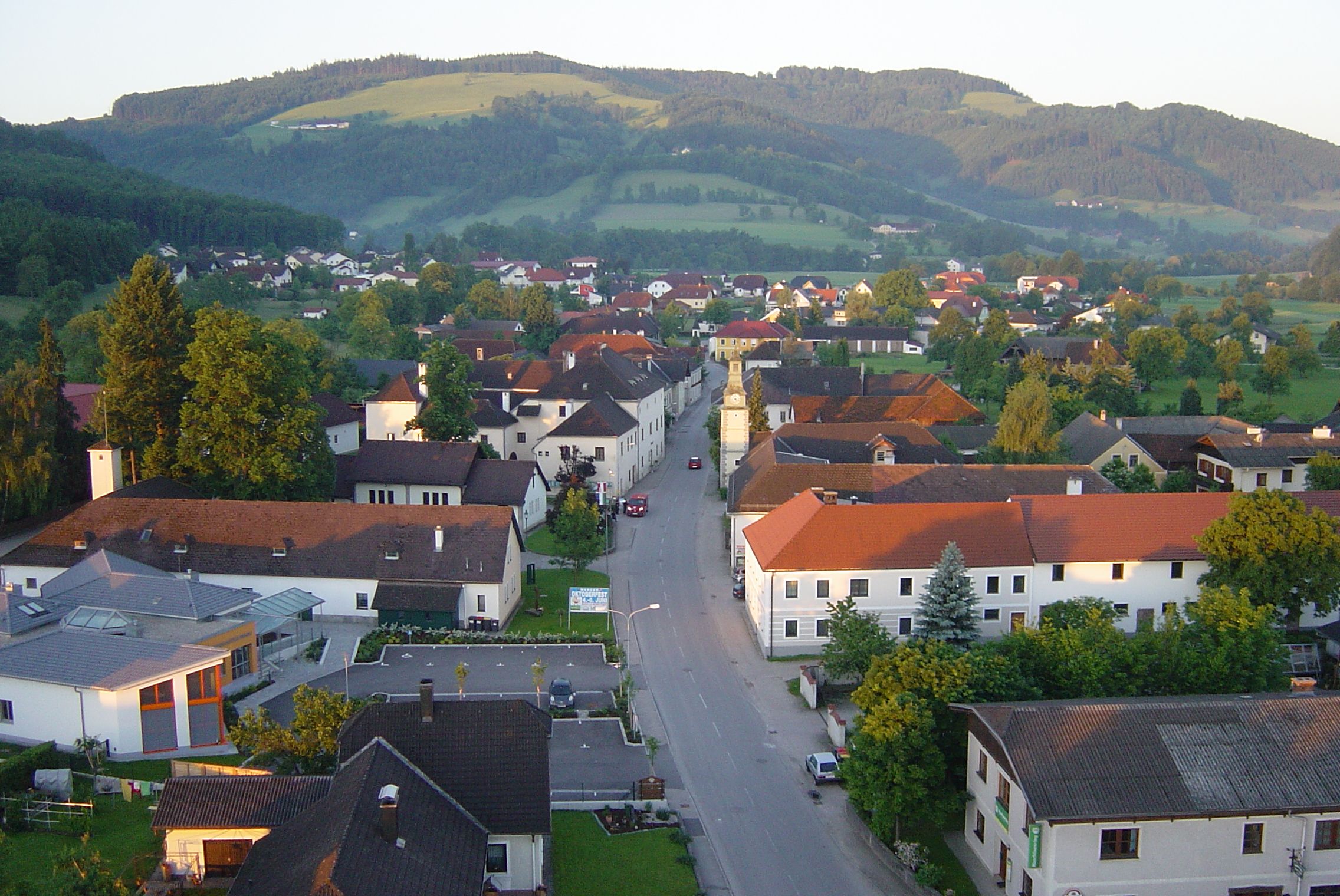 Luftaufnahme eines Dorfes mit roten Dächern und grüner Landschaft im Hintergrund.