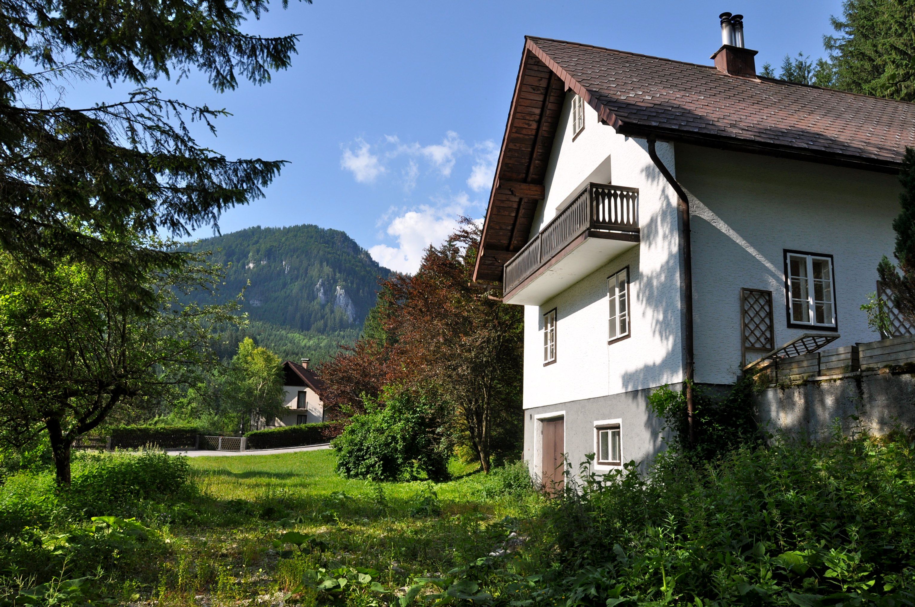 Ein weißes Ferienhaus mit Balkon vor einer Berglandschaft und grünem Garten.