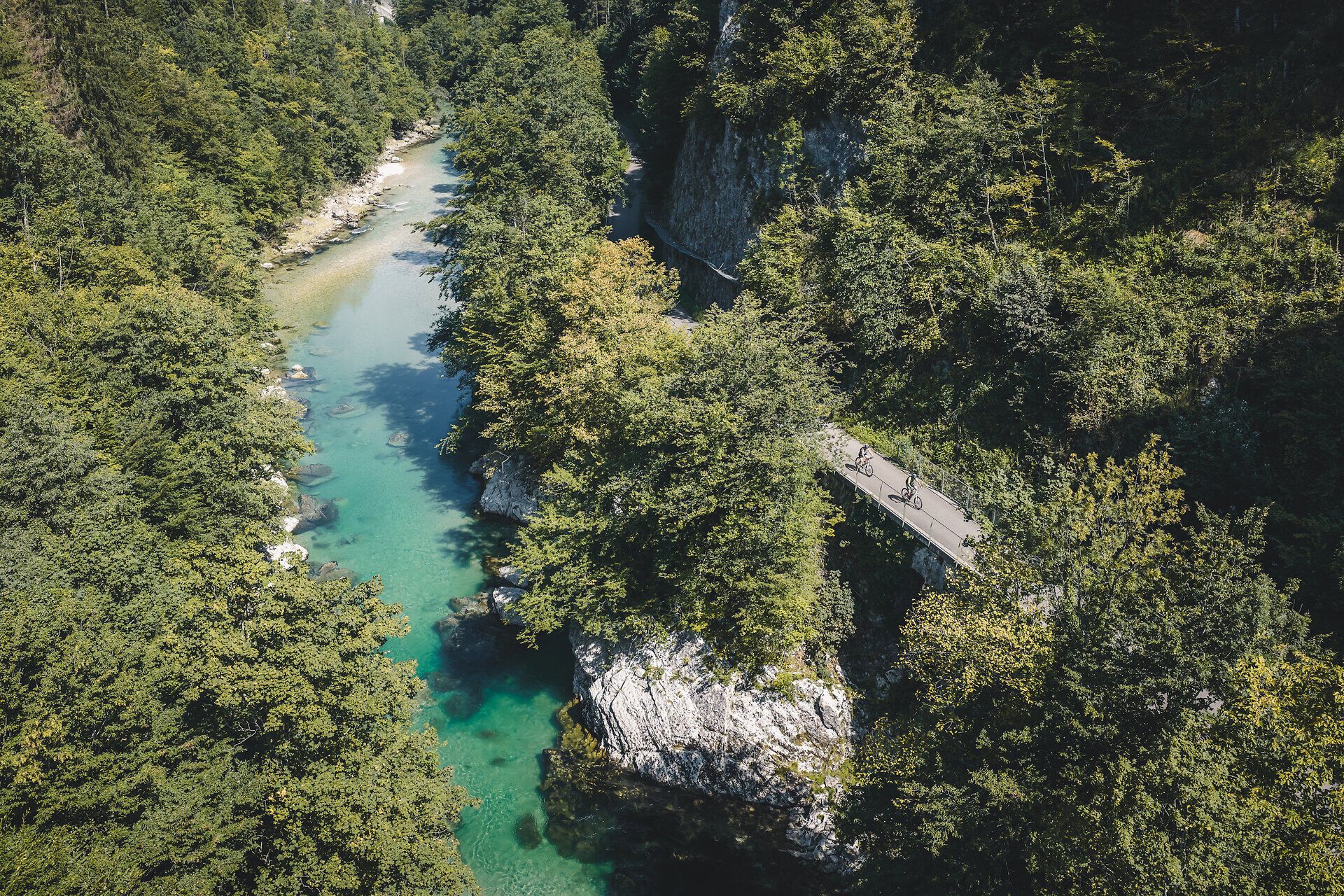 Luftaufnahme der Ybbs, umgeben von bewaldeter Vegetation und daneben zwei Radfahrenden am Ybbstalradweg