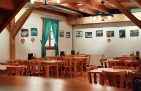 Innenansicht eines rustikalen Gastraums mit Holzmöbeln und Bildern an der Wand.