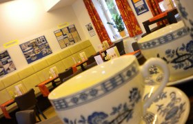 Innenansicht eines Cafés mit Teetassen im Vordergrund und dekorierten Wänden im Hintergrund.