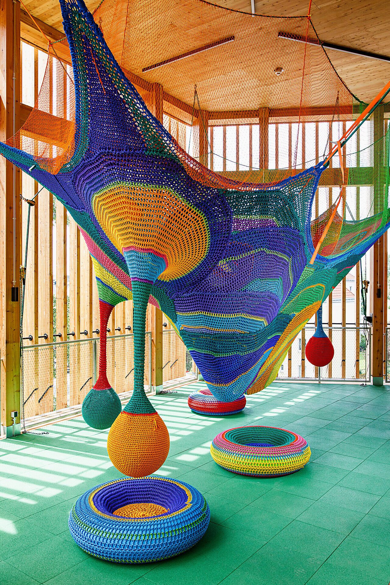 In einem bunten Raum voller kreativer Energie schwingen farbenfrohe Netze einladend durch die Luft. Kinder können hier spielerisch ihre Fantasie entfalten und in eine Welt voller Kunst und Abenteuer eintauchen.