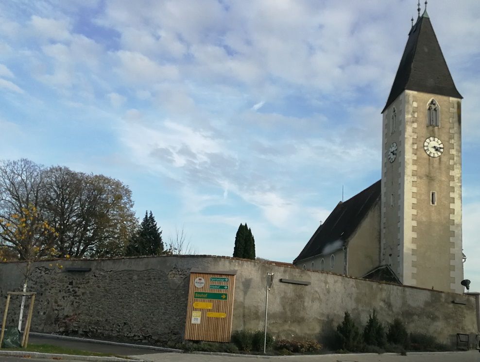 Kirche mit Turm und Uhr in Hafnerbach, umgeben von einer Mauer.