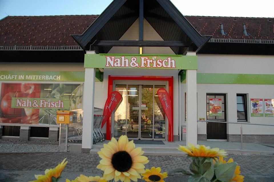 Eingang eines Nah & Frisch Supermarkts mit Sonnenblumen im Vordergrund.