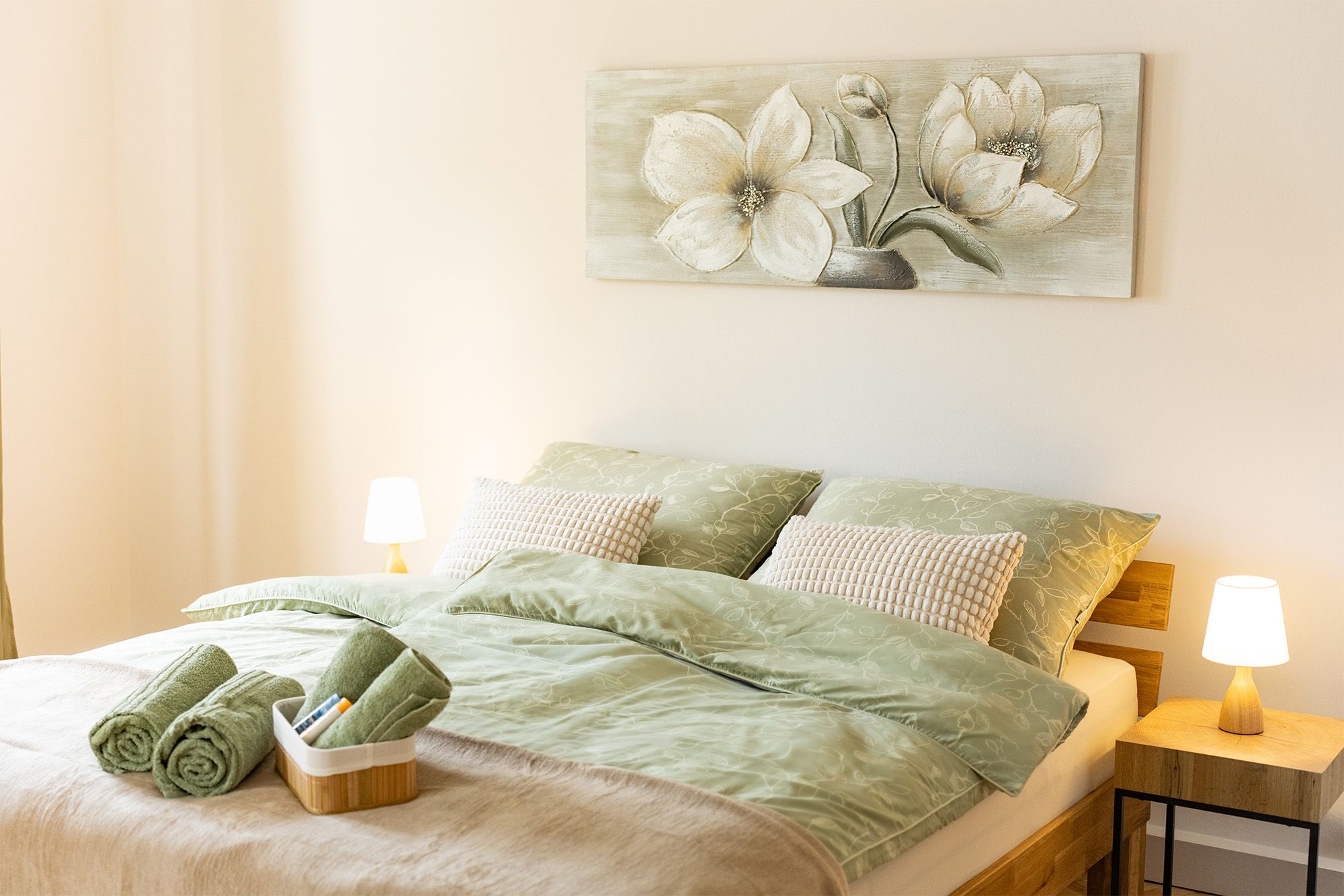 Gemütliches Schlafzimmer in der Ferienwohnung Turmblick mit Doppelbett, grüner Bettwäsche, Nachttischlampen und Blumenbild an der Wand.