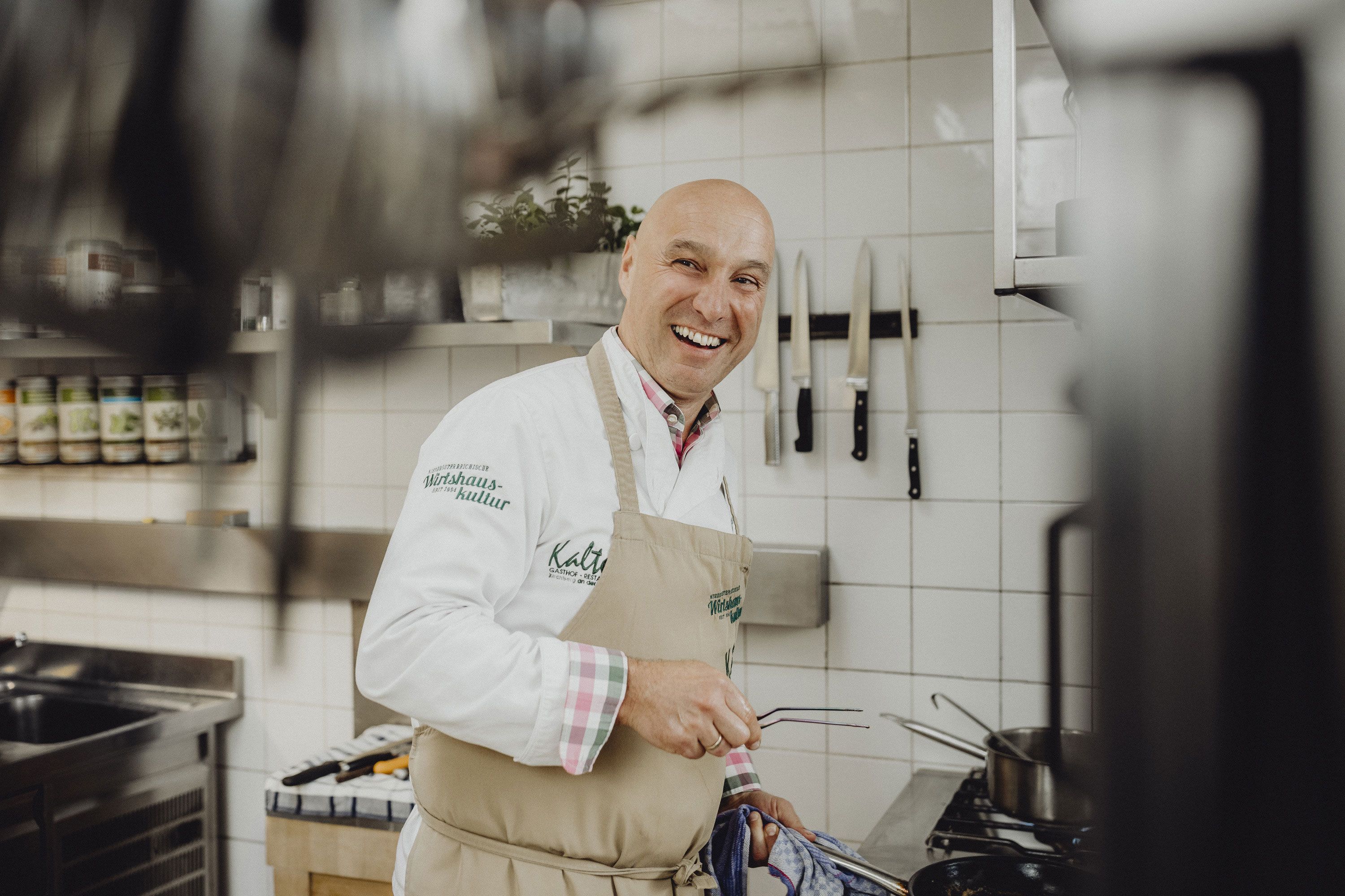 Ein lachender Koch in einer professionellen Küche mit Messern an der Wand.
