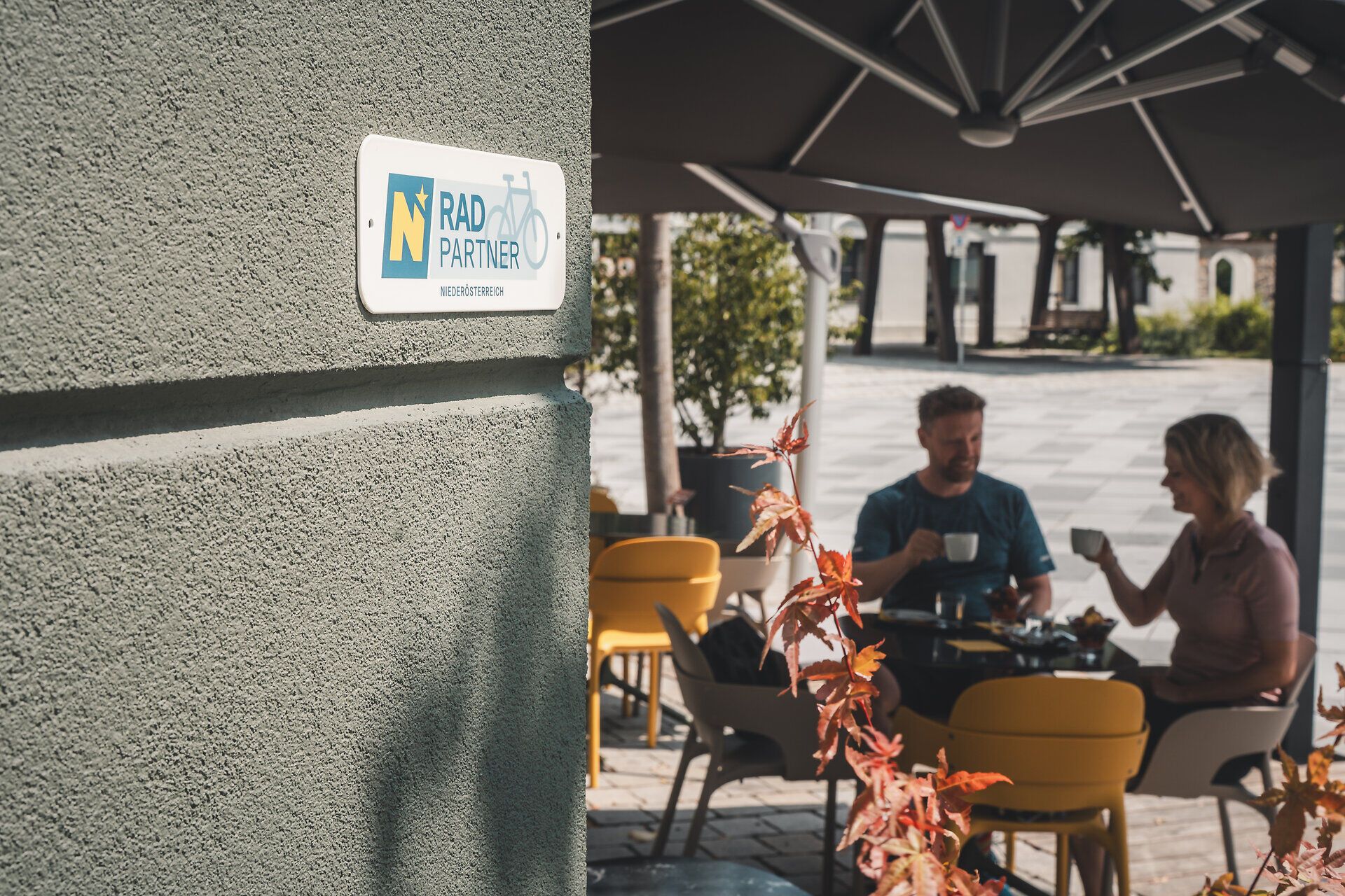 Ein Paar sitzt bei einem Café, im Vordergrund ist das Radpartner-Schild an der Wand montiert