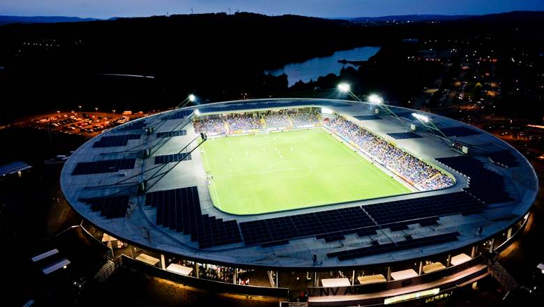 Luftaufnahme eines beleuchteten Fußballstadions bei Nacht.