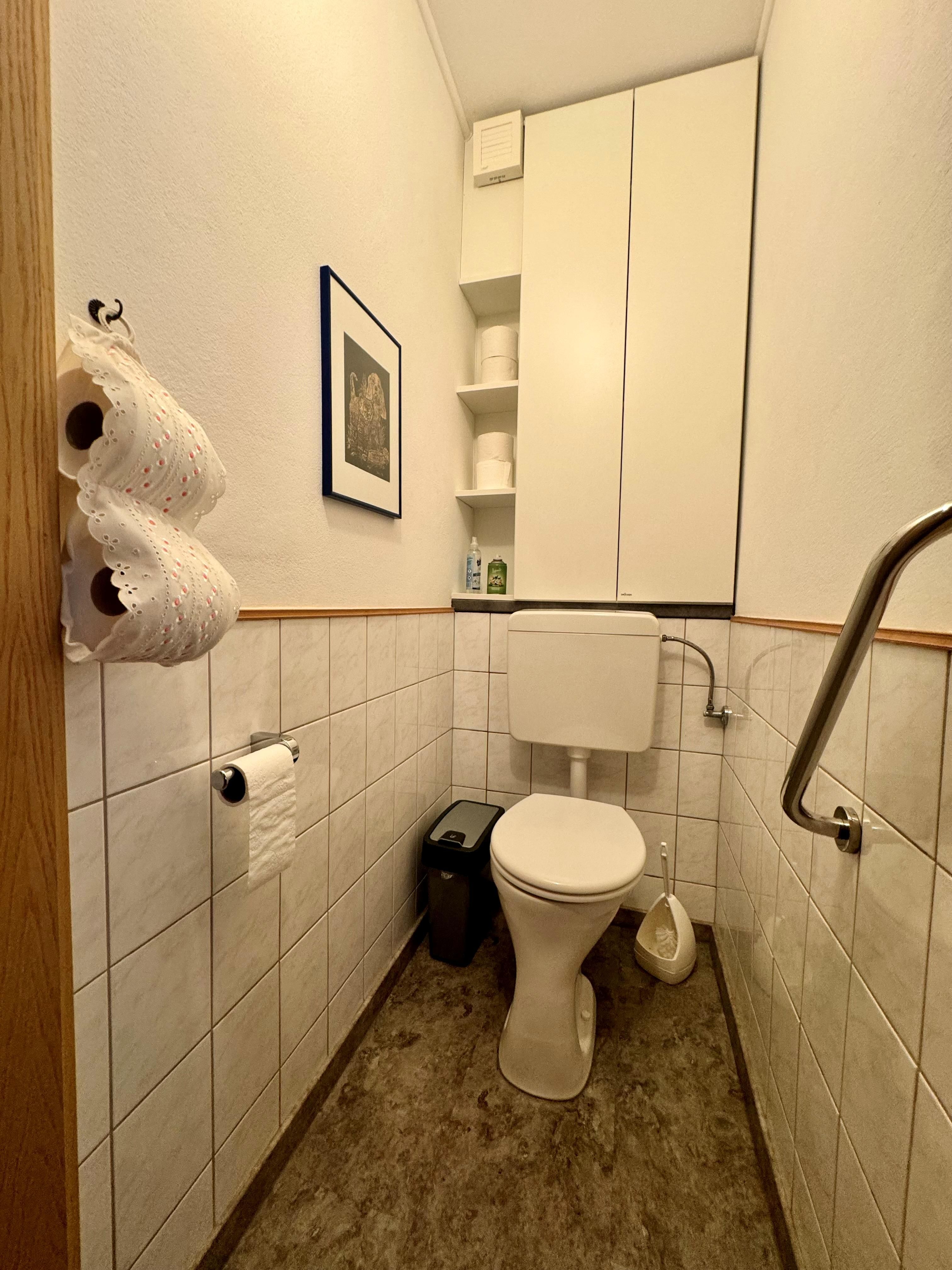 Kleines Badezimmer mit Toilette, weißen Fliesen und einem Schrank.