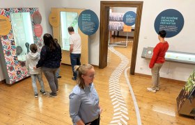 Menschen in einem Museum betrachten interaktive Ausstellungen mit Texttafeln und Exponaten.