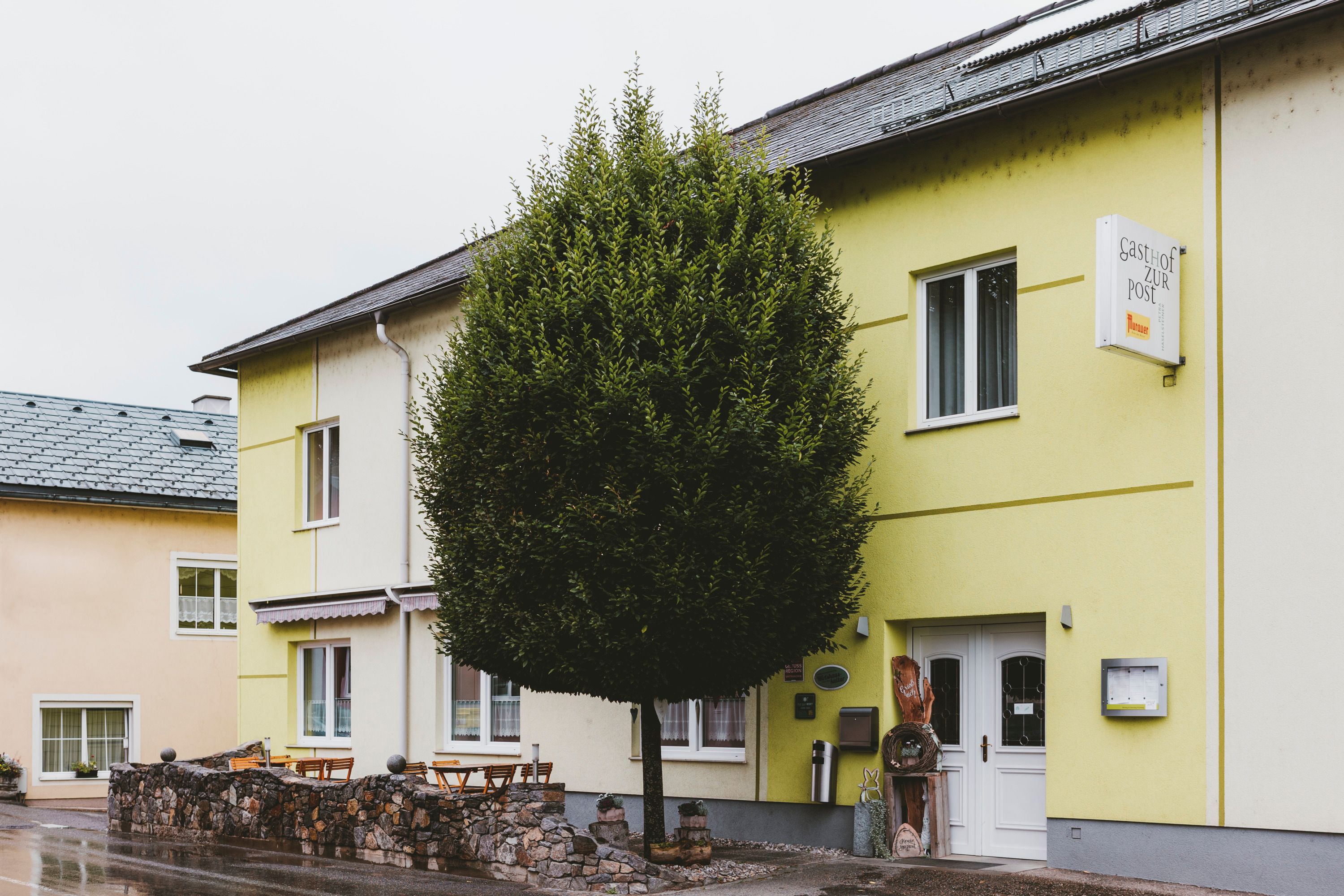 Außenansicht eines Gasthofs mit gelber Fassade und Baum davor.