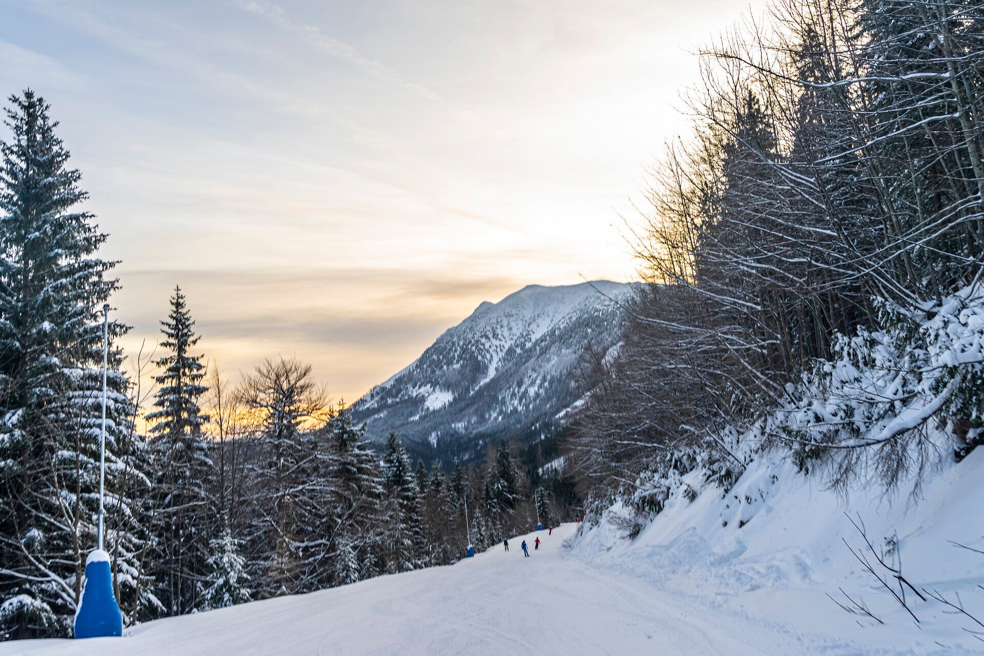 Die sanften Hänge des Ötschers sind in eine glitzernde Schneedecke gehüllt, während die ersten Sonnenstrahlen den Himmel in warmen Farben erleuchten. Skifahrer gleiten fröhlich die Pisten hinunter und genießen die frische, klare Winterluft in dieser idyllischen Berglandschaft.