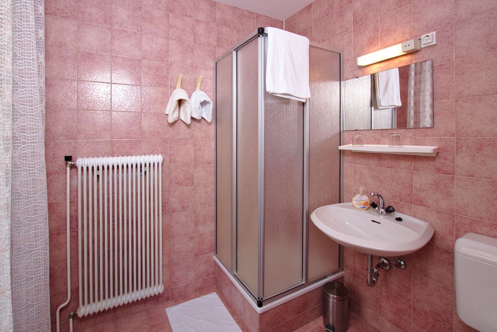 Badezimmer mit rosa Fliesen, Duschkabine, Waschbecken und Heizkörper.
