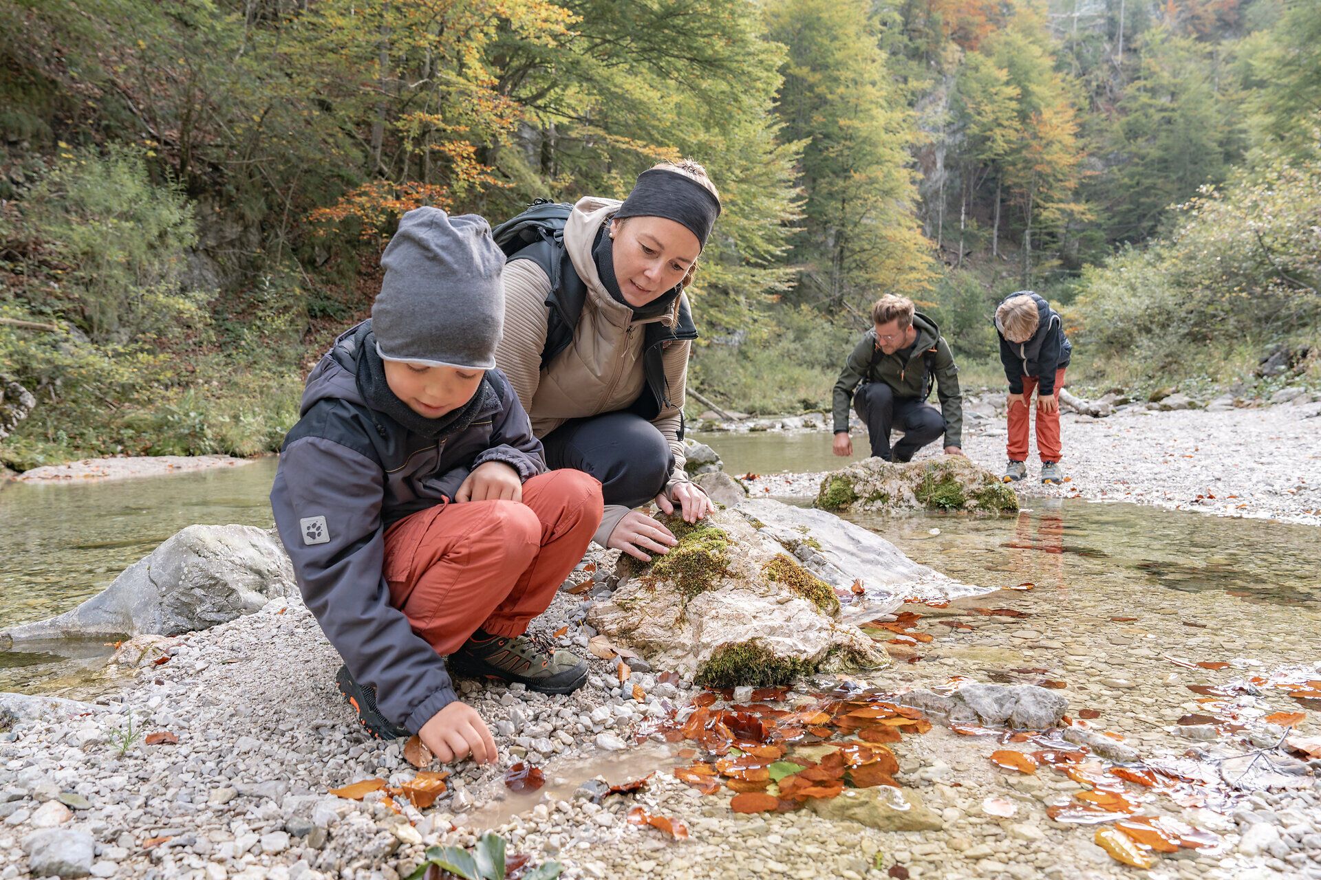In der malerischen Kulisse des Naturparks Ötscher-Tormäuer erkunden Familien gemeinsam die Schönheit der Natur. Kinder sammeln bunte Blätter und kleine Steine am Ufer eines klaren Baches, während die Erwachsenen die frische Herbstluft genießen. Diese harmonische Verbindung von Spiel und Entdeckung schafft unvergessliche Erinnerungen inmitten der beeindruckenden Landschaft.