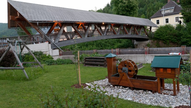 Covered wooden bridge over a river with a small water wheel in the foreground.