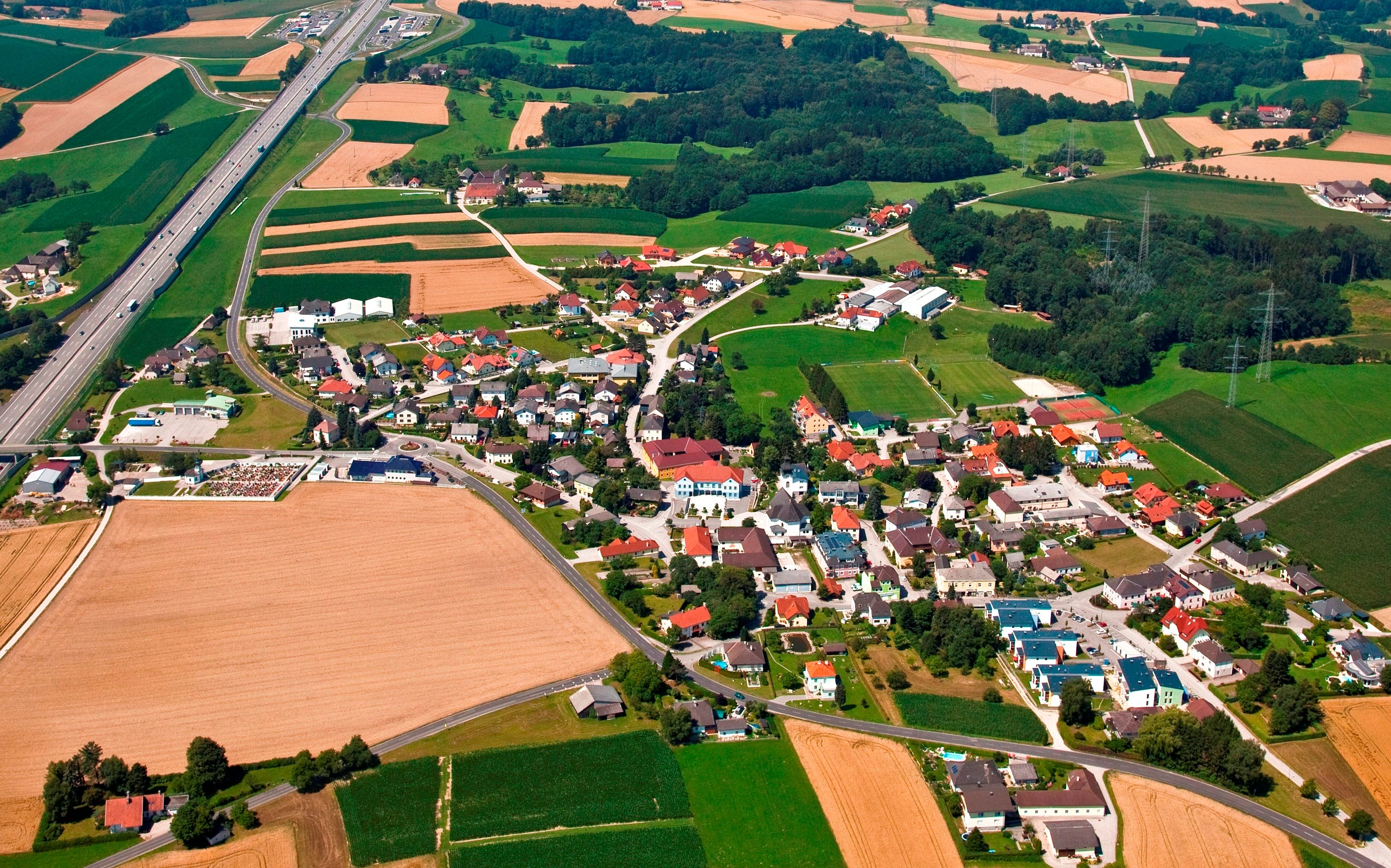 Luftaufnahme eines Dorfes mit Feldern und einer Autobahn.