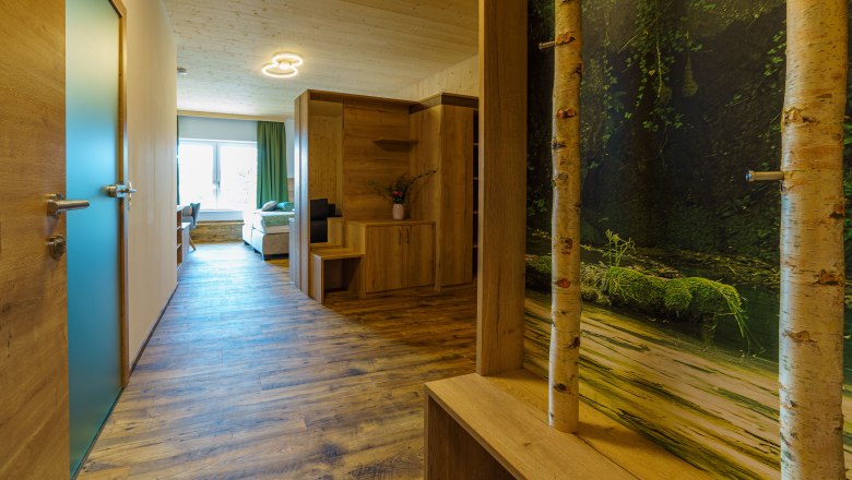 Innenansicht eines modernen Apartments mit Holzboden, Holzmöbeln und einem großen Fenster.