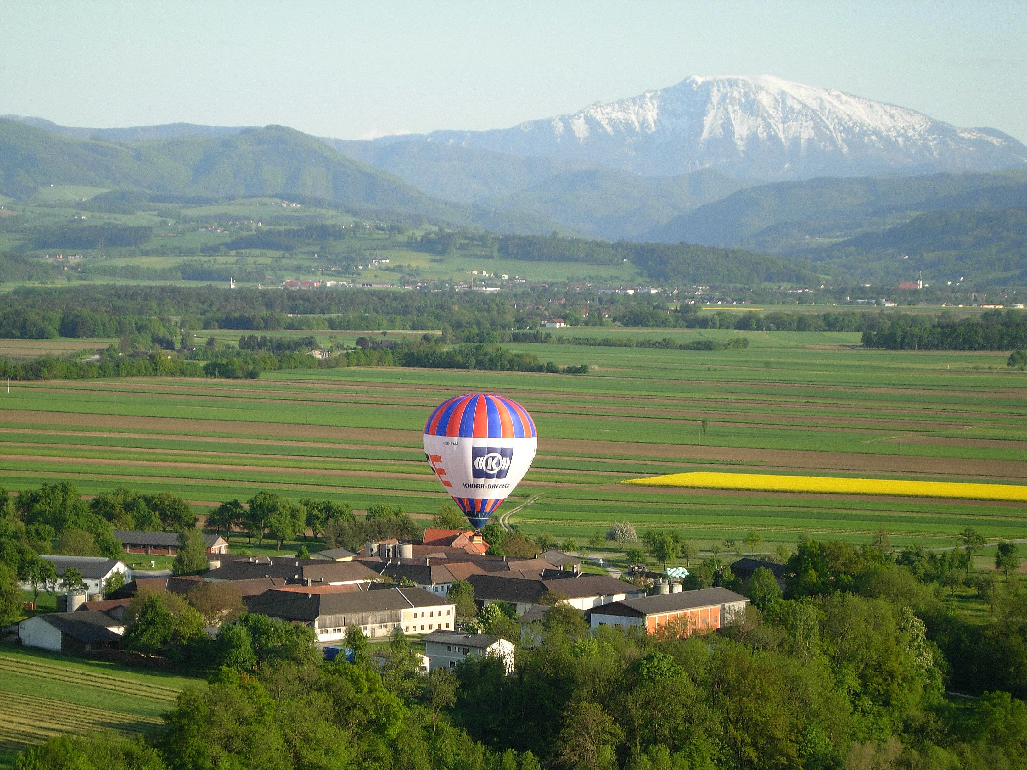 Heißluftballon über einer ländlichen Landschaft mit Bergen im Hintergrund.