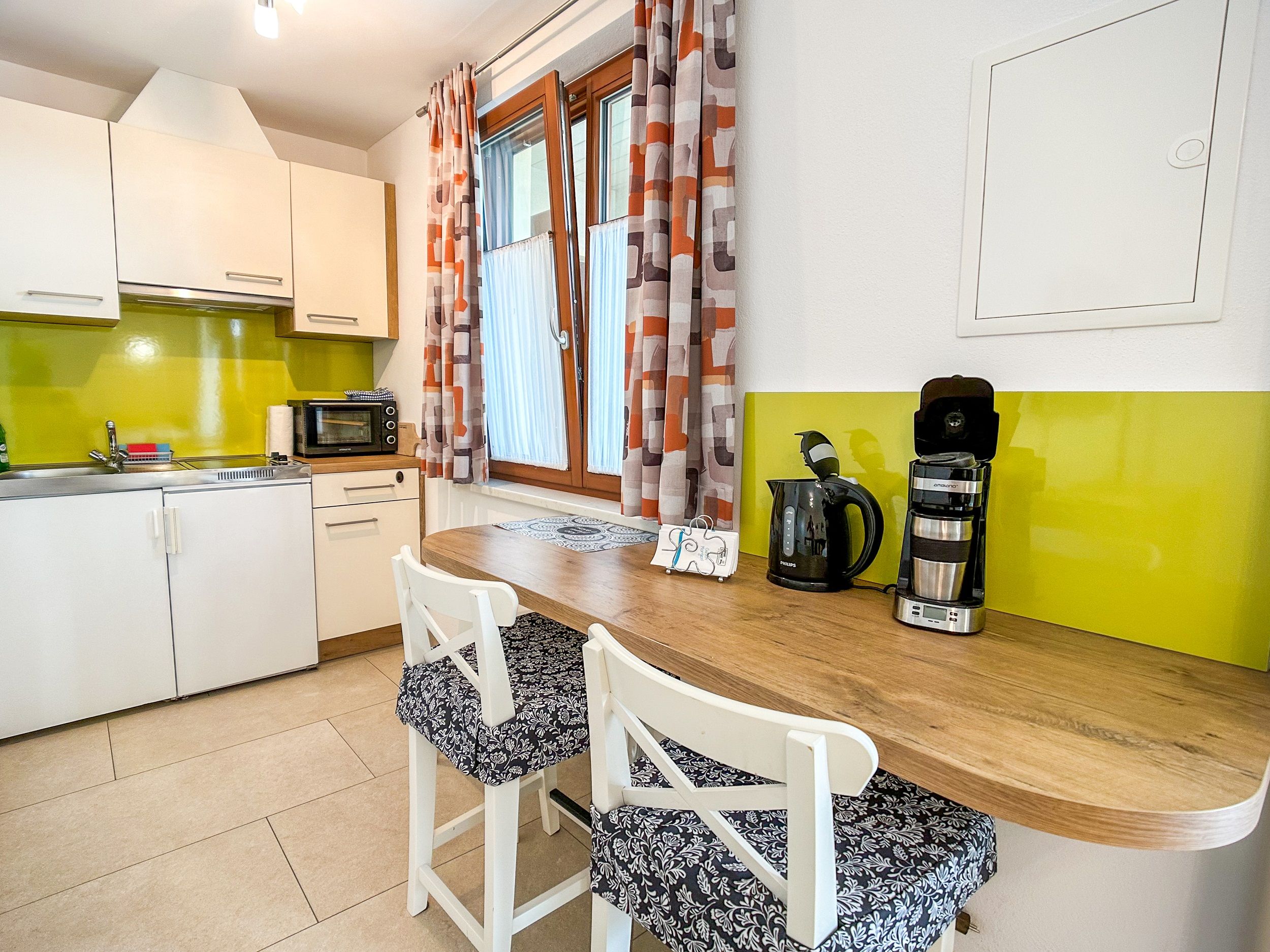 Moderne Küche mit grüner Rückwand, weißen Schränken, Holztheke und Kaffeemaschine.