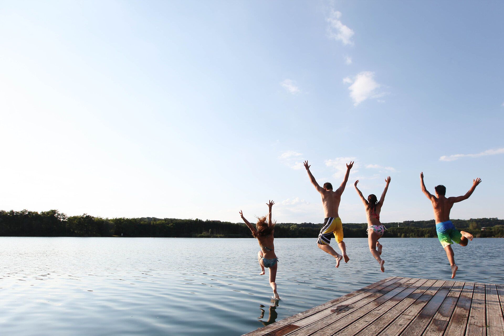 An einem strahlend schönen Sommertag springen fröhliche Menschen ins erfrischende Wasser der Viehofner Seen. Die unbeschwerte Atmosphäre und das glitzernde Wasser laden zum Baden und Entspannen ein, während die sanften Wellen die Ufer umspielen.