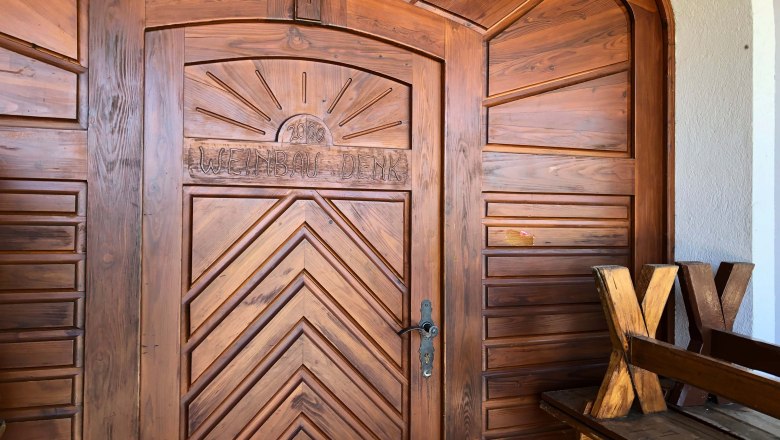 Holztür mit der Aufschrift 'Weinbau Denk' und einer Sonne darüber.