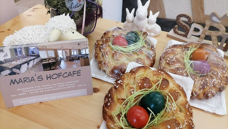 Drei Osterkränze mit bunten Eiern auf einem Tisch, daneben eine Karte von Maria's Hofcafe und Osterdekoration.