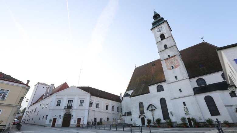 Parish church with clock tower and adjoining buildings on an empty square.
