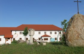 A farm with a red roof and a large stone with a cross in the foreground.