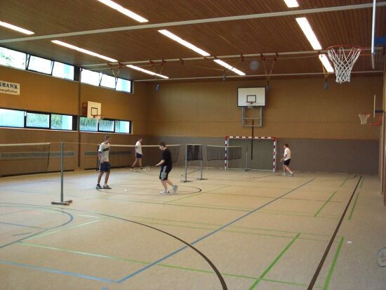Innenansicht einer Sporthalle mit Badmintonspielern und Basketballkorb.
